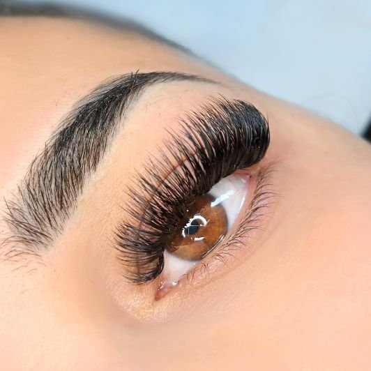Olho esquerdo de cor castanho de uma mulher olhando para a câmera com extensão de cílios volume híbrido