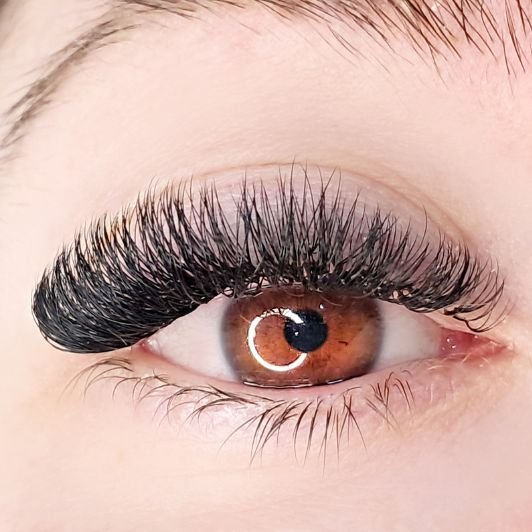 Mulher com olhos castanhos olhando para a câmera com extensão de cílios volume russo em seu olho.
