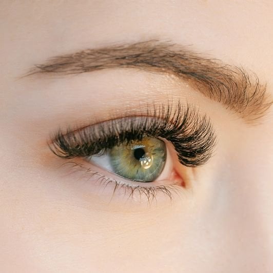 Mulher com olhos verdes olhando para o horizonte com extensão de cílios fio a fio nos cílios.