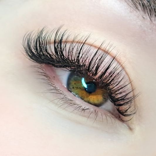 Mulher com olhos esverdeados e mel com extensão de cílios híbrido nos fios.