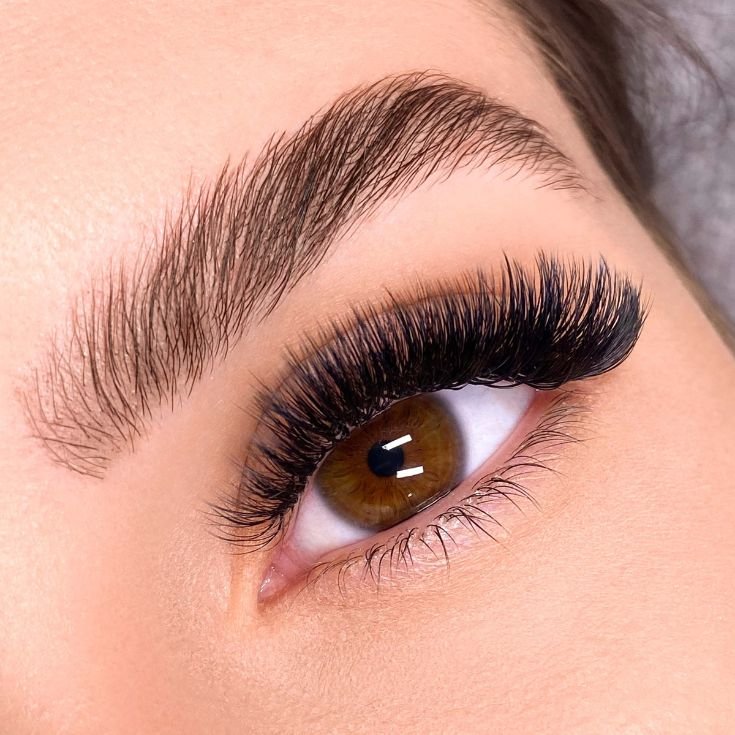 Mulher com olhos castanhos escuros e extensão de cílios volume russo em seu olho.
