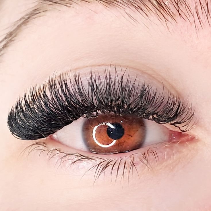Mulher com olhos castanhos olhando para a câmera com extensão de cílios volume russo em seu olho.