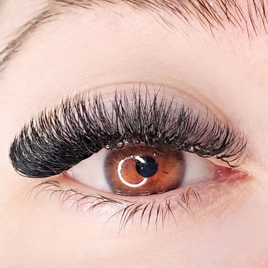 Mulher com olhos castanhos olhando para a câmera com extensão de cílios volume russo em seu olho.