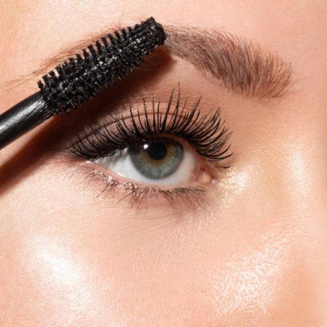 Mulher de olhos claros aplicando mscara para sobrancelha com escovinha destacando clios volumosos e