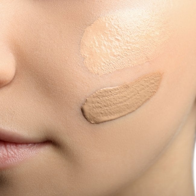 Rosto de uma mulher com swatches de base na bochecha.