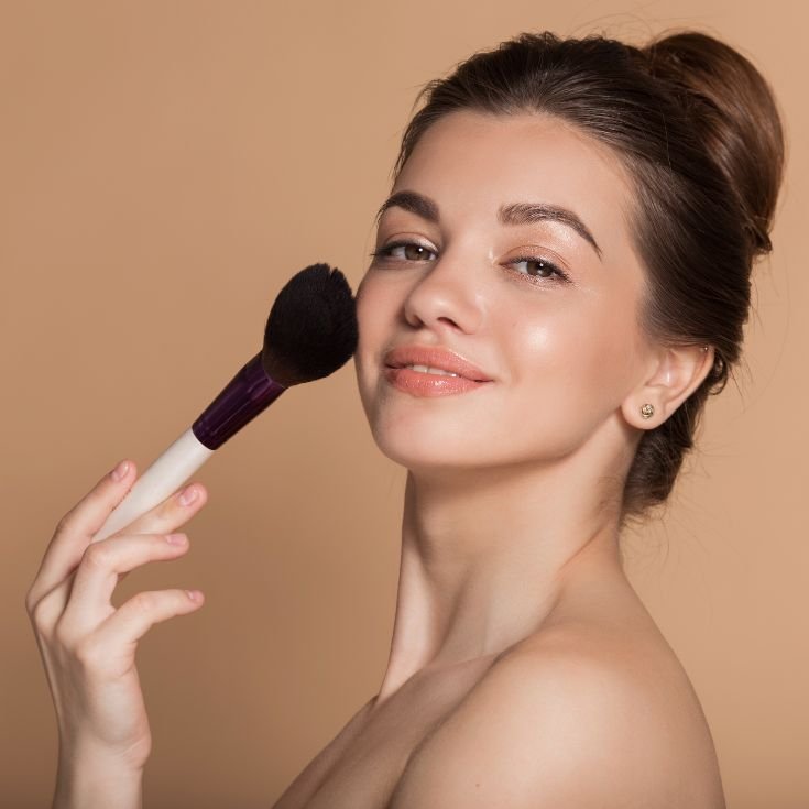 Jovem mulher sorridente aplica o blush em pó com um pincel aplicador