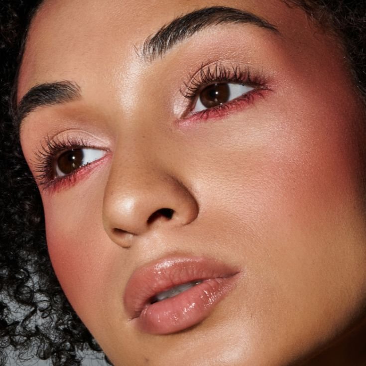 Jovem mulher negra com blush líquido aplicado em seu rosto como parte de sua maquiagem