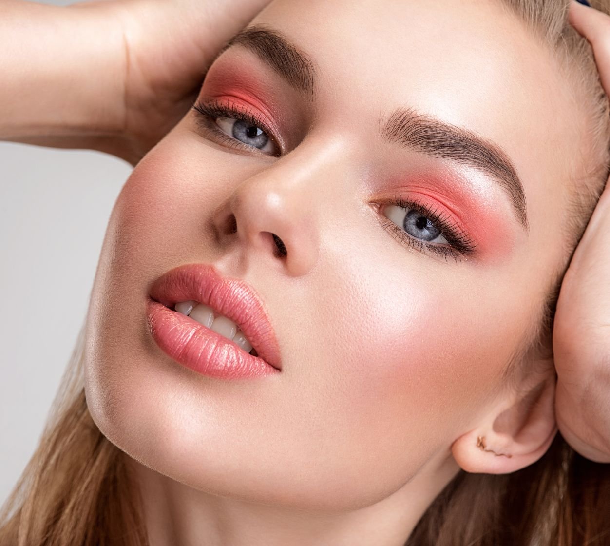 Mulher caucasiana com uma maquiagem cor coral e blush cremoso leve