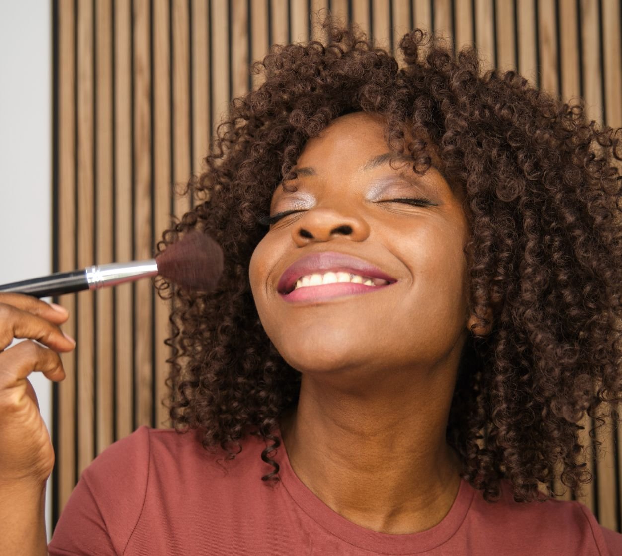 Mulher negra e sorridente aplica o blush em pó na sua pele do rosto