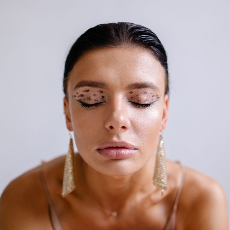 Mulher com os olhos fechados exibindo uma maquiagem estilo oncinha nos olhos.
