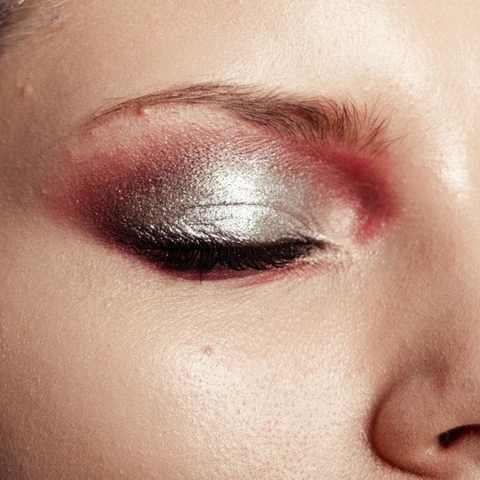 Olhos maquiados com uma camada generosa de sombra prata em toda a pálpebra e esfumado com uma sombra cintilante acobreada nas extremidades.