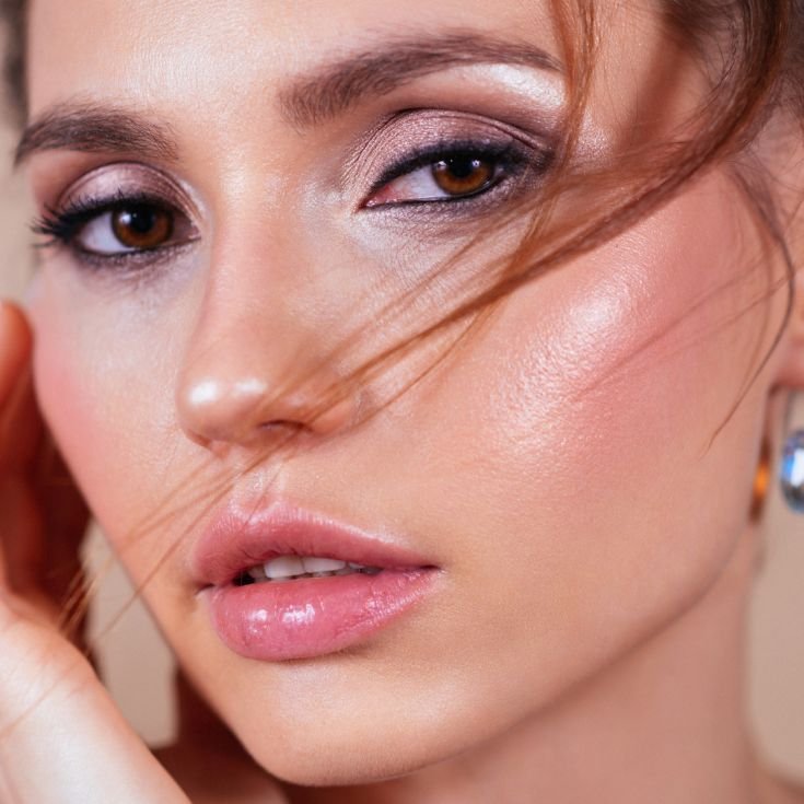 Mulher usando maquiagem inspirada no estilo anos 2000 de moda sutil, com sobrancelhas e cílios naturais mas usando gloss e sombra cintilante e lápis esfumado na linha d’água.