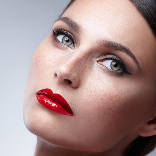 Mulher com maquiagem leve nos olhos, blush leve nas bochechas, sardas marrons e um batom vermelho marcante.